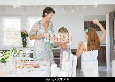 Donna in piedi con le sue figlie a giocare a un tavolo da pranzo Foto Stock