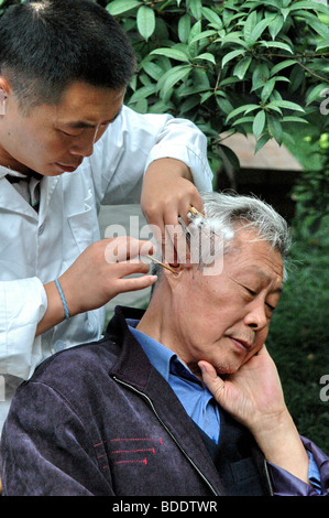 Cina, Locale medicina cinese, orecchio pulizia in un parco Foto Stock