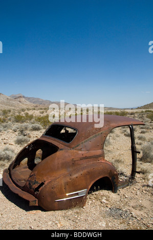 Rusty bruciato a guscio di una metà di un auto nel deserto Foto Stock