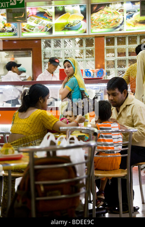 Donna indiana cliente aspetta per fast food service al contatore. Ristorante Haldirams, Delhi. India. Una famiglia è mangiare in primo piano. Foto Stock