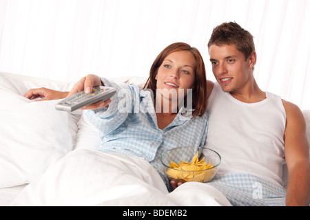 Giovane donna e uomo disteso nel letto a guardare la televisione e mangiare patatine Foto Stock