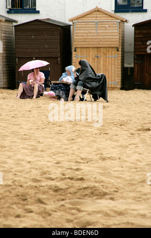 Località balneare inglese: vacanzieri seduti sulla spiaggia sotto la pioggia a Broadstairs, Kent, Regno Unito Foto Stock