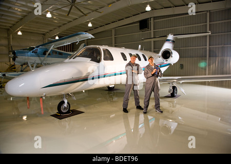 Due aereo meccanica in piedi accanto a piccoli aerei in hangar Foto Stock