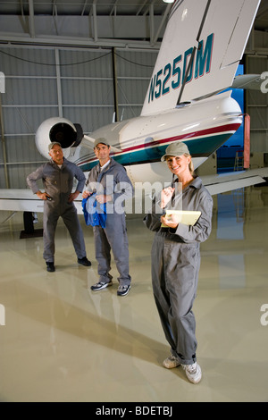 Tre aereo meccanica in piedi accanto a piccoli aerei in hangar Foto Stock