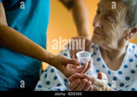 Donna anziana in carrozzina getting medicina da un infermiere Foto Stock