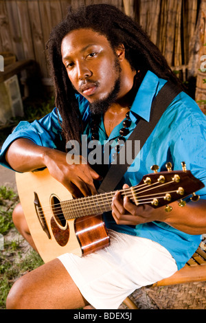 Ritratto di giovane uomo giamaicano con dreadlocks tenendo la chitarra su isola tropicale Foto Stock