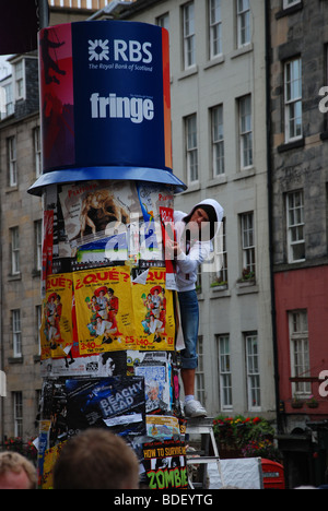 L'uomo mette i manifesti per la Edinburgh Fringe su un cartellone Foto Stock