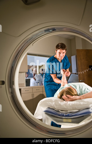 Paziente sdraiato su CAT scan macchina mentre healthcare lavoratore prende impulso Foto Stock