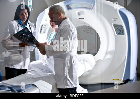 I radiologi guardando i risultati dei test con paziente in prossimità dello scanner TC Foto Stock