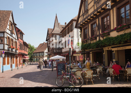 Scena di strada con cafe' sul marciapiede in città medievale sul vino Alsaziano rotta. Kaysersberg, Alsazia, Haut-Rhin, in Francia, in Europa. Foto Stock