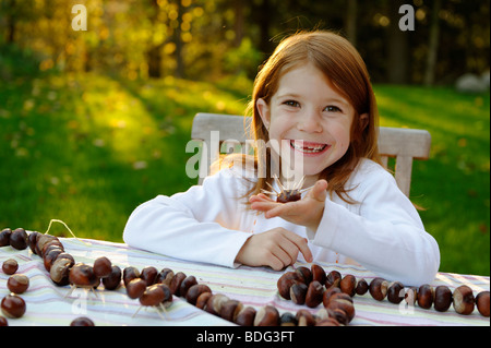 Ragazza è giocare in giardino con castagne e castagni, riccio, figure di castagno Foto Stock