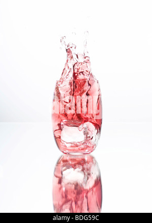 Cubetti di ghiaccio di cadere in un bicchiere riempito con liquido rosso Foto Stock