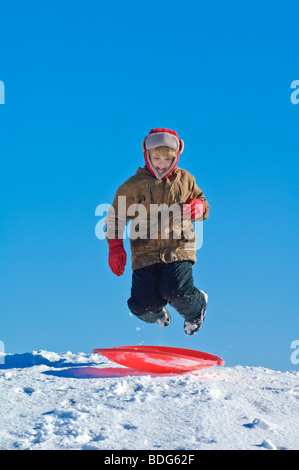 Un giovane salti su una slitta su una neve Wisconsin hillside in novembre. Foto Stock