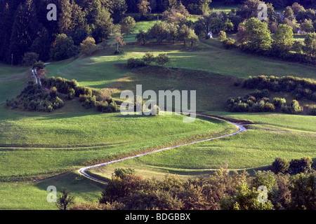 Una strada di ghiaia avvolgimento il verde delle colline di seguito Zavrh Trojanah pri, vicino Trojane, Slovenia. Foto Stock