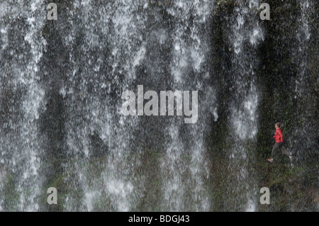 Una donna trail running dietro una cascata a Silver Falls State Park, Oregon, Stati Uniti d'America. Foto Stock