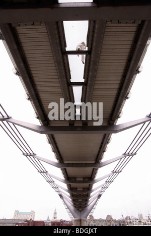 London Millenium Bridge dal Tamigi foreshore in acque basse, una persona visibile attraverso la maglia aperta del ponte di coperta Foto Stock