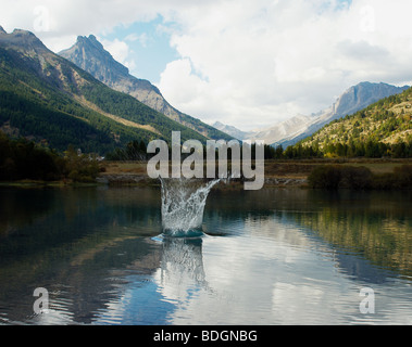 Una vista delle Alpi con un lago in primo piano. uno spruzzo di acqua saltando dal lago Foto Stock