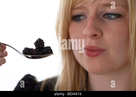 I giovani di 20 anni donna bionda con un cucchiaio di more fresche con una diffida volto Foto Stock