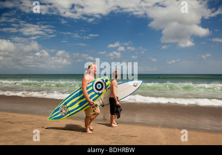 Indonesia Bali Kuta Beach, padre e figlio surfers camminando lungo il bordo delle acque con tavole da surf Foto Stock