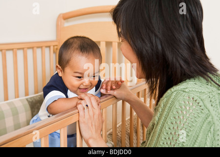 Baby all'interno di culle, tenendo le mani con la madre Foto Stock