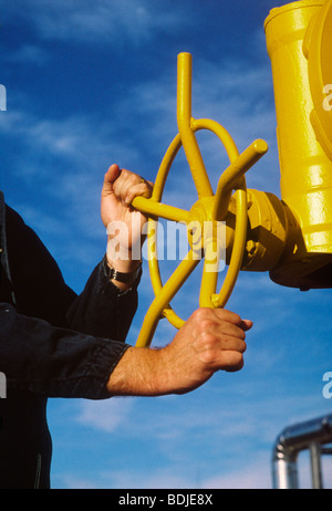 Mani ruotando la valvola gialla ruota, impianto industriale Foto Stock