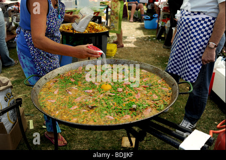 Donna cucinare aggiunge sale in una grande padella di paella di essere cucinati al Festival di Brunswick a Hove Brighton Regno Unito Foto Stock