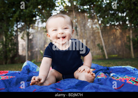 Baby sitting su una coperta al di fuori Foto Stock