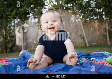 Baby sitting su una coperta al di fuori Foto Stock