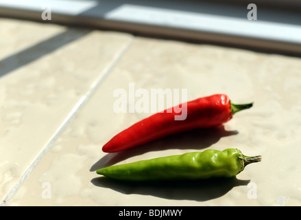 Il verde e il peperoncino rosso sul davanzale della maturazione al sole Foto Stock