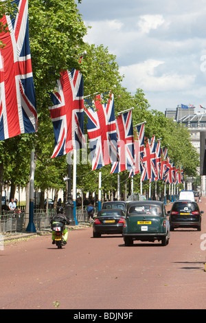 Fila di Unione Jack bandiere lungo il Mall, a Londra come black cabs passano al di sotto. Foto Stock