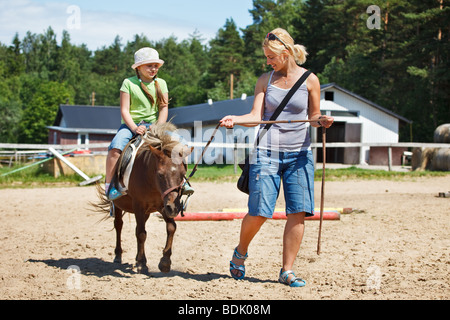 Poco ragazza sorridente e cavalcare pony Foto Stock