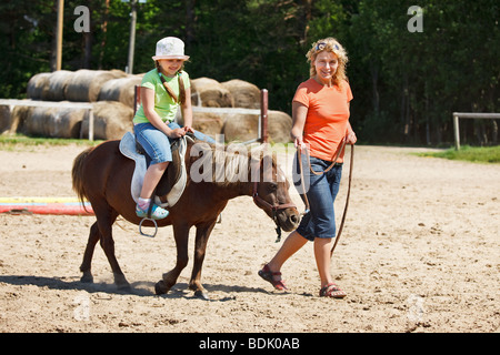 Poco ragazza sorridente e cavalcare pony Foto Stock