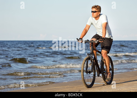 Uomo Bicicletta Equitazione in spiaggia lungo il mare Foto Stock