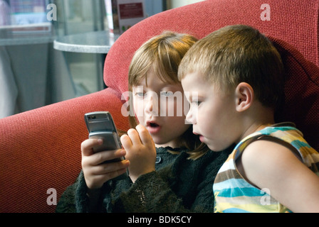 Scioccato fratello e sorella e utilizzando un telefono cellulare per visualizzare annuncio dalla Organizzazione Mondiale della Sanità circa il cancro di cervello Foto Stock