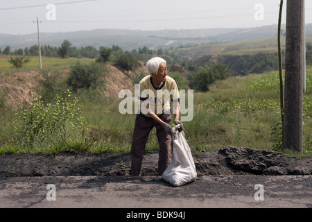 DATONG, nella provincia di Shanxi, Cina - Agosto 2007: una povera donna raccoglie il carbone è sceso dal passaggio del carbone di autocarri per l'uso per il carburante. Foto Stock