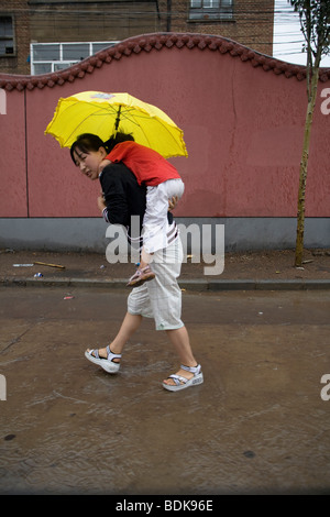 DATONG, nella provincia di Shanxi, Cina - Agosto 2007: una giovane madre porta in sé il giovane figlia sulle sue spalle sotto il suo ombrello Foto Stock