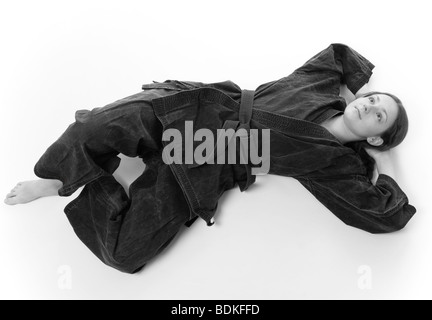 Nudi ragazza in uniforme nera giace piatta sul retro nel pavimento, gettate le mani e gambe incrociate, bianco-e-nero Foto Stock