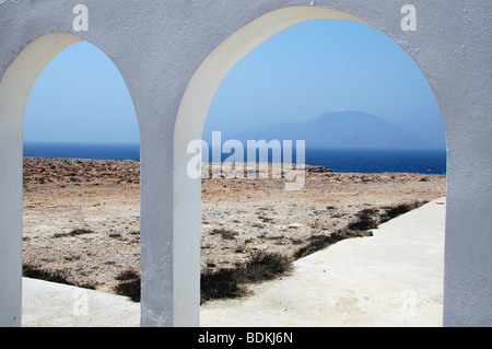 Le arcate esterne di un vecchio, imbiancato chiesa di Agia Theodoros sull'isola greca di Karpathos; l'isola di Kasos, Grecia, in background. Foto Stock