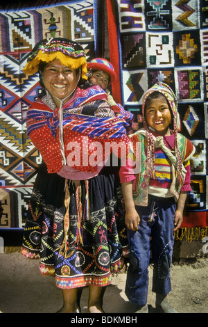 Il quechua donna indiana con bambini in piedi di fronte a un peruviano textile display, Pisac, Perù, Sud America Foto Stock