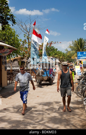 Indonesia, Lombok, Gili Trawangan, turisti e cavallo cidomo powered taxi sulla strada della spiaggia Foto Stock