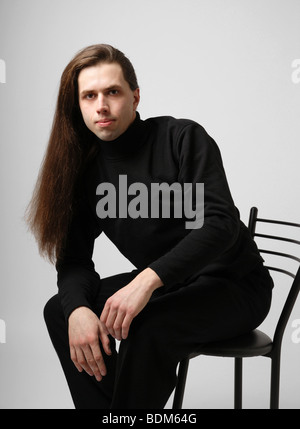 Ben coltivate compagno seduto in maglione nero e pantaloni Foto Stock