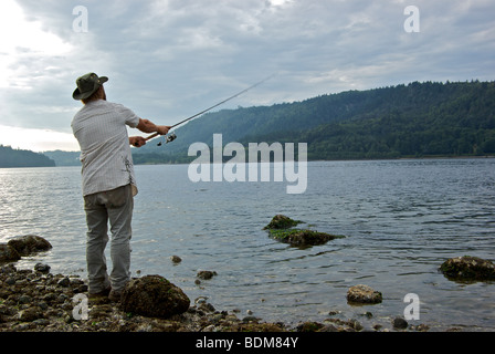 L'uomo spin casting esca mentre la pesca in spiaggia per il rosa salmone in asta sfocatura del movimento Foto Stock