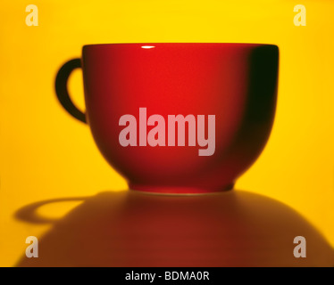 Una immagine drammatica di una rossa tazza da caffè con ombra contro una forte sfondo giallo Foto Stock