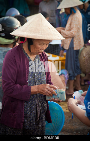 Un vietnamita vecchia donna lo scambio di denaro al mercato indossando un cappello conico Foto Stock