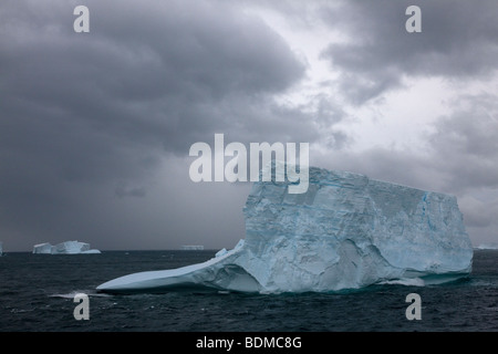 Il grande blu Iceberg galleggiante a nord nell'Oceano del Sud nei pressi di Georgia del sud le isole sotto eerie moody tempestoso cielo nuvoloso Foto Stock