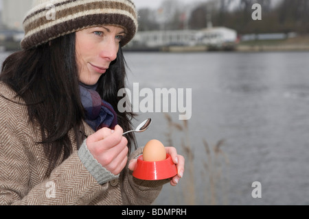 Giovane donna, 30-35 anni, mangiando un breakfest uovo in una fredda giornata invernale presso il Canale di Kiel, Schleswig-Holstein, Germania, Europa Foto Stock