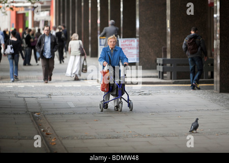 Un parzialmente disabili donna anziana utilizzando un telaio provvisto di ruote a piedi nella zona centrale di Londra, Regno Unito Foto Stock