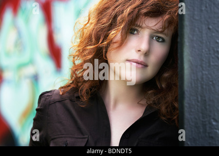 Ritratto di un giovane, i capelli rossi donna, appoggiata contro un graffiti-parete spruzzato Foto Stock