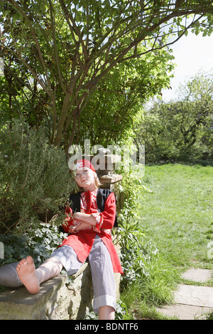 Giovane ragazzo (7-9) indossando il costume pirata seduta con bracci incrociati in giardino Foto Stock