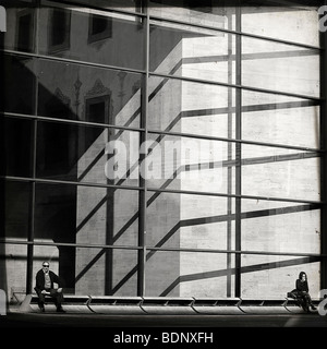 Due persone sedute al di fuori di un edificio moderno in vetro in un ambiente urbano Foto Stock